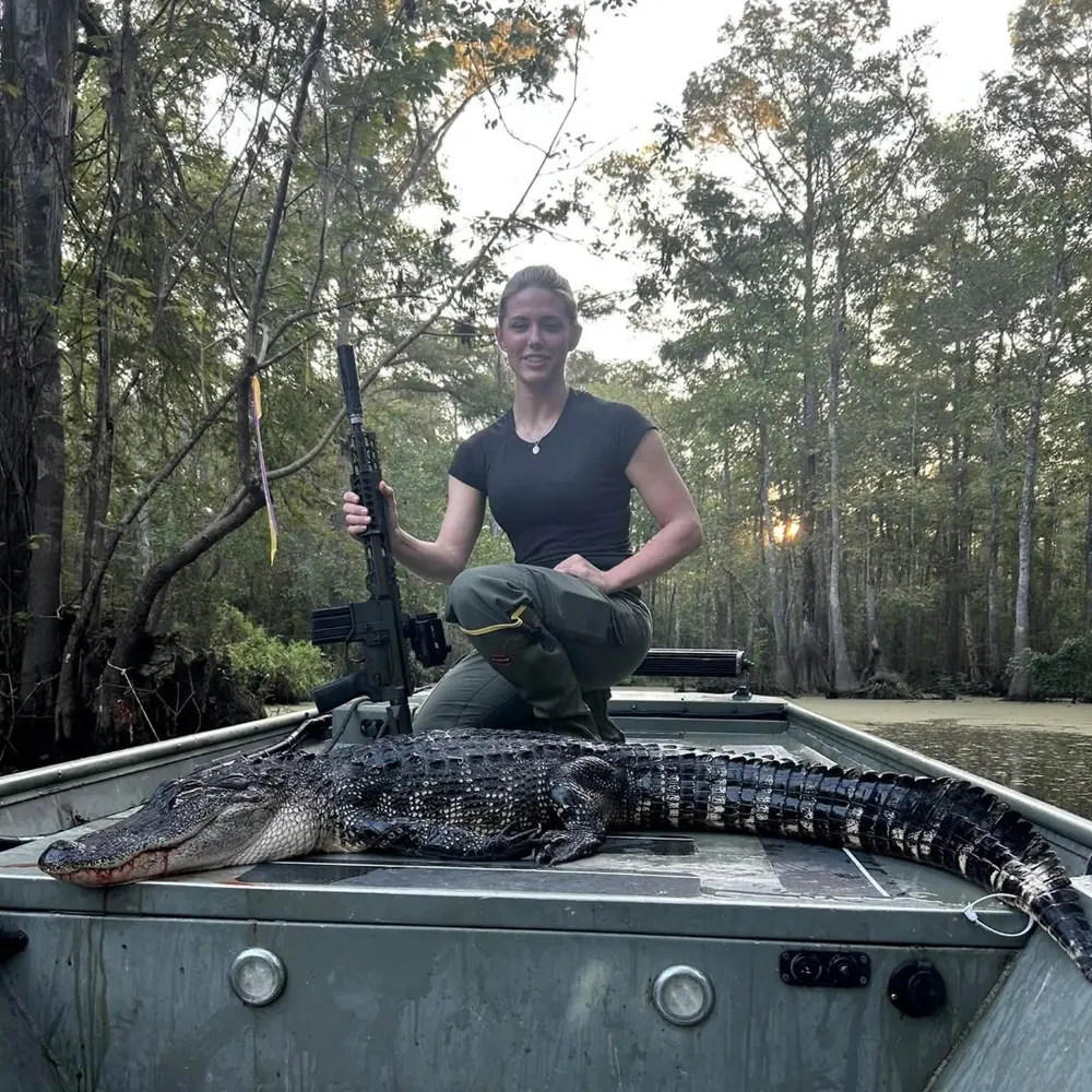 Hunter kneeling behind an alligator in a jon boat at sunrise in a Louisiana cypress swamp